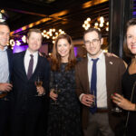 Five guests dressed in formal attire smile while holding drinks at the CHiPS Annual Gala 2025 in Brooklyn.