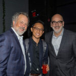 Three men dressed in suits smile together at the CHiPS Annual Gala 2025 in Brooklyn, one holding a red drink.
