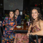 Three guests seated at a table smiling at the CHiPS Annual Gala 2025 in Brooklyn, surrounded by floral centerpieces and wine glasses.