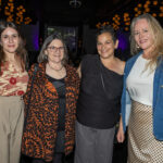 Four women standing together and smiling at the 2025 CHiPS Annual Gala in Brooklyn, dressed in elegant evening outfits with patterned tops and dresses.