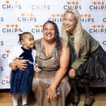 Two women and a small child smiling together in front of the CHiPS step-and-repeat banner at the 2025 CHiPS Annual Gala in Brooklyn.