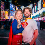 @mauricios_log dressed as Spider-Man “Bag-Man,” wearing a blue Fantastic Four bodysuit with the number 4 emblem and a paper bag mask, crouching at the New York Comic Con Time Square Meetup in Time Square, New York City.