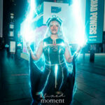 @tiarabreecosplay dressed as Storm from X-Men, wearing a black and gold costume with flowing cape and silver hair, surrounded by glowing blue lightning effects at the New York Comic Con Time Square Meetup in Times Square, New York City.