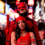 @insomniacwebslinger dressed as Daredevil standing behind @earthtotorii dressed as Elektra, both wearing red costumes, posing together in Times Square at the New York Comic Con Times Square Meetup.