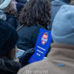 Person holding a blue NYC Inauguration 2026 program in a seated crowd outside New York City Hall during the January 1, 2026 inauguration.