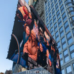 Large outdoor video screen outside New York City Hall displaying members of the crowd during the January 1, 2026 inauguration, with tall buildings rising behind the screen.