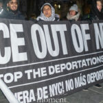 Protesters holding a large banner that reads “ICE Out of NYC – Stop the Deportations Now” during a nighttime demonstration in New York City.