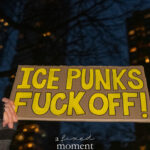 Hand-painted protest sign reading “ICE Punks Fuck Off!” in bold yellow lettering, held at night in New York City.