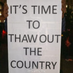 Printed protest sign reading “It’s Time to Thaw Out the Country,” held at a nighttime rally in New York City.