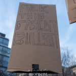 Cardboard protest sign reading “Fuck This Fascist Bullshit” held above a crowd during a winter protest in New York City.