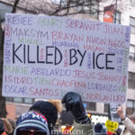 Handwritten protest sign reading “Killed by ICE” surrounded by victims’ names, held above a crowd during a winter protest in New York City.