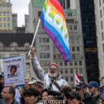 Protester holding a rainbow “LOVE” flag above a crowd at the Hands Off protest on January 11, 2026, near 60th Street and Fifth Avenue in New York City.
