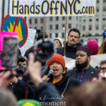 New York City Council Member Alexa Avilés speaking into a microphone at the Hands Off protest on January 11, 2026, near 60th Street and Fifth Avenue in Manhattan.