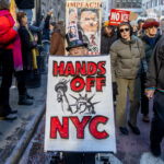 Protester holding a “Hands Off NYC” sign with an “Impeach” image of Donald Trump during the Hands Off protest on January 11, 2026, in Midtown Manhattan.