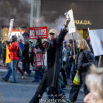 Protesters marching with “No Wars! Hands Off Latin America” signs past the Prada storefront during the Hands Off protest on January 11, 2026, in Midtown Manhattan.