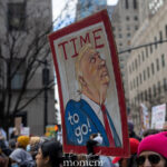 Hand-painted cartoon protest sign reading “TTME to go!” held during a march in New York City.