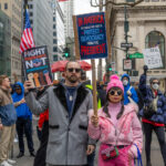 Two protesters holding signs reading “Fight Ignorance Not Immigrants” and “Protect Democracy From the President” while marching in New York City.
