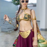Princess Leia slave cosplay wearing gold armor top, purple skirt, chain prop, and sunglasses at Dragon Con 2025 in Atlanta, GA. Cosplayer @dtmarrone.