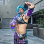 Jinx cosplay with long blue braided wig, black crop top, purple striped pants, and oversized purple rocket launcher prop at Dragon Con 2025 in Atlanta, GA.