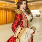A striking female Captain Hook poses inside the convention atrium at Dragon Con 2025 in Atlanta, GA, holding a polished brass hook while wearing an ornate red and gold period gown. Cosplayer: @asta.darling | Event: @dragoncon | https://www.dragoncon.org