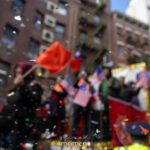 Colorful confetti floats in front of blurred spectators waving American and Chinese flags during the Lunar New Year Parade in Chinatown, New York City.