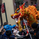 A colorful red and gold dragon head is lowered toward a child in the crowd during the Lunar New Year Parade in Chinatown, New York City.