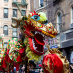 A colorful Chinese dragon head with gold, red, and green detailing is held above the crowd during the Lunar New Year Parade in Chinatown, New York City.