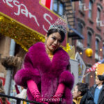 A parade float performer wearing a silver tiara, magenta fur stole, and pink gloves poses during the Lunar New Year Parade in Chinatown, New York City.