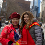 Julie Menin stands beside a parade attendee wearing a red traditional jacket and hat during the Lunar New Year Parade in Chinatown, New York City.