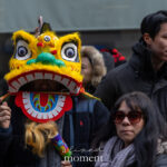 A parade spectator holds a bright yellow lion dance mask with large eyes and an open mouth during the Lunar New Year Parade in Chinatown, New York City.