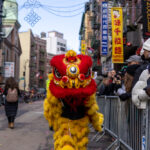 A performer wearing a yellow and red lion dance costume walks along the street during the Lunar New Year Parade in Chinatown, New York City.