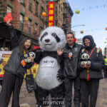 A large panda mascot wearing a βPanda Mobileβ logo stands with parade attendees holding small panda plush toys during the Lunar New Year Parade in Chinatown, New York City.
