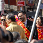 Mayor Zohran Mamdani smiles while wearing a red sash and speaking with attendees during the Lunar New Year Parade in Chinatown, New York City.