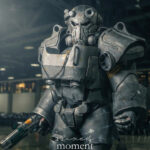 Cosplayer wearing detailed Fallout Power Armor holds a prop weapon on the convention floor during Awesome Con.