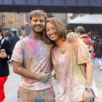 Two participants covered in colorful Holi powder smile and pose together during the Festival of Colors celebration at Pier 17 in New York City.