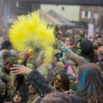 Bright yellow Holi powder thrown into the air above a crowd of participants during the Festival of Colors celebration at Pier 17 in New York City.