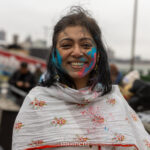 Participant smiling with blue and pink colored powder on their face during the Holi celebration at Pier 17 in New York City.