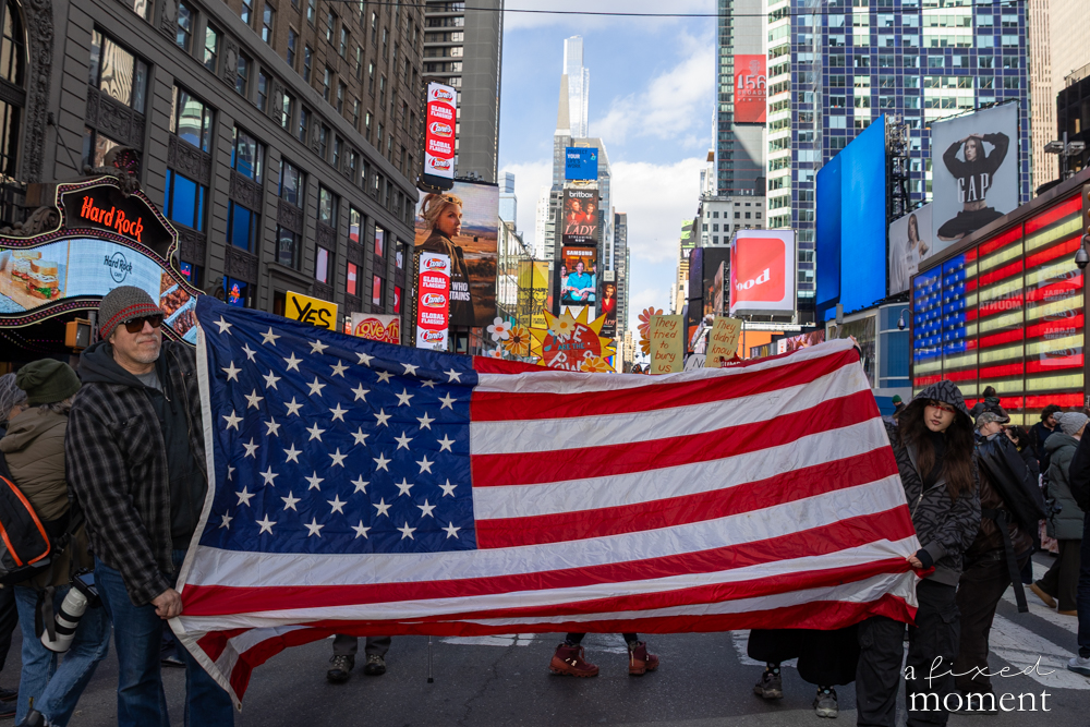 Participants carry a large American flag through Times Square during the No Kings protest in New York City.