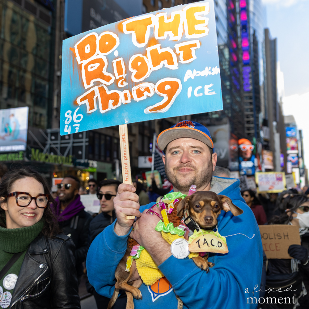 A protester holds a Do the Right Thing sign while carrying a small dog in costume during the No Kings protest in New York City.