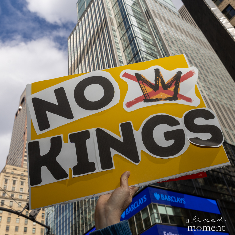 A No Kings protest sign is raised against the Midtown Manhattan skyline.