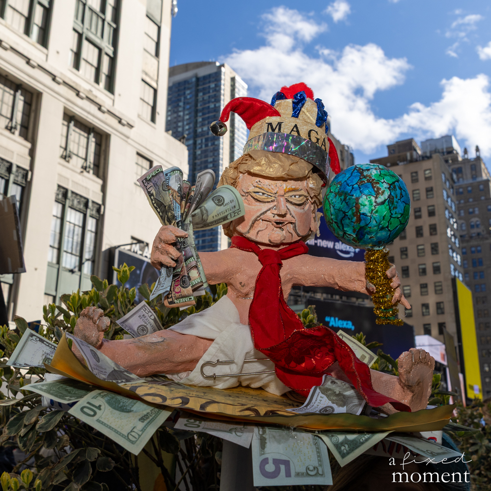A satirical papier-mâché figure with a MAGA crown holds money and a globe during the No Kings protest in Manhattan.