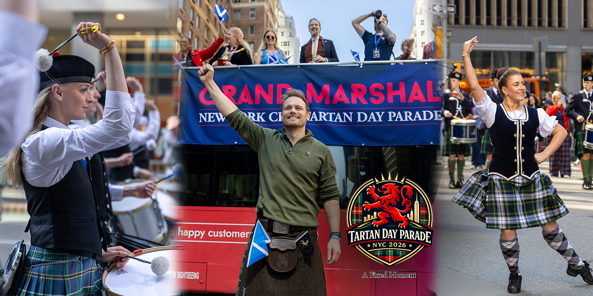 Sam Heughan stands in front of a Grand Marshal banner on a parade bus, raising his fist while holding a bottle of whisky as Highland dancers and drummers perform on Sixth Avenue in New York City.