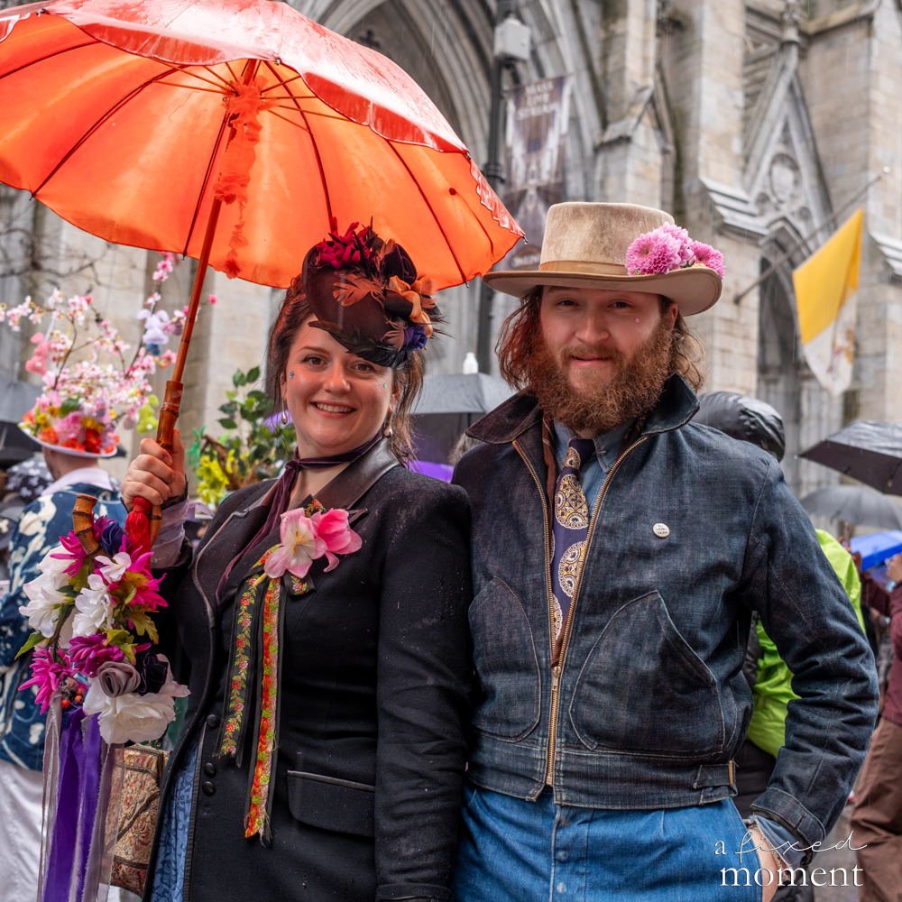 A couple posing under an umbrella at the Easter Parade and Bonnet Festival in New York City.