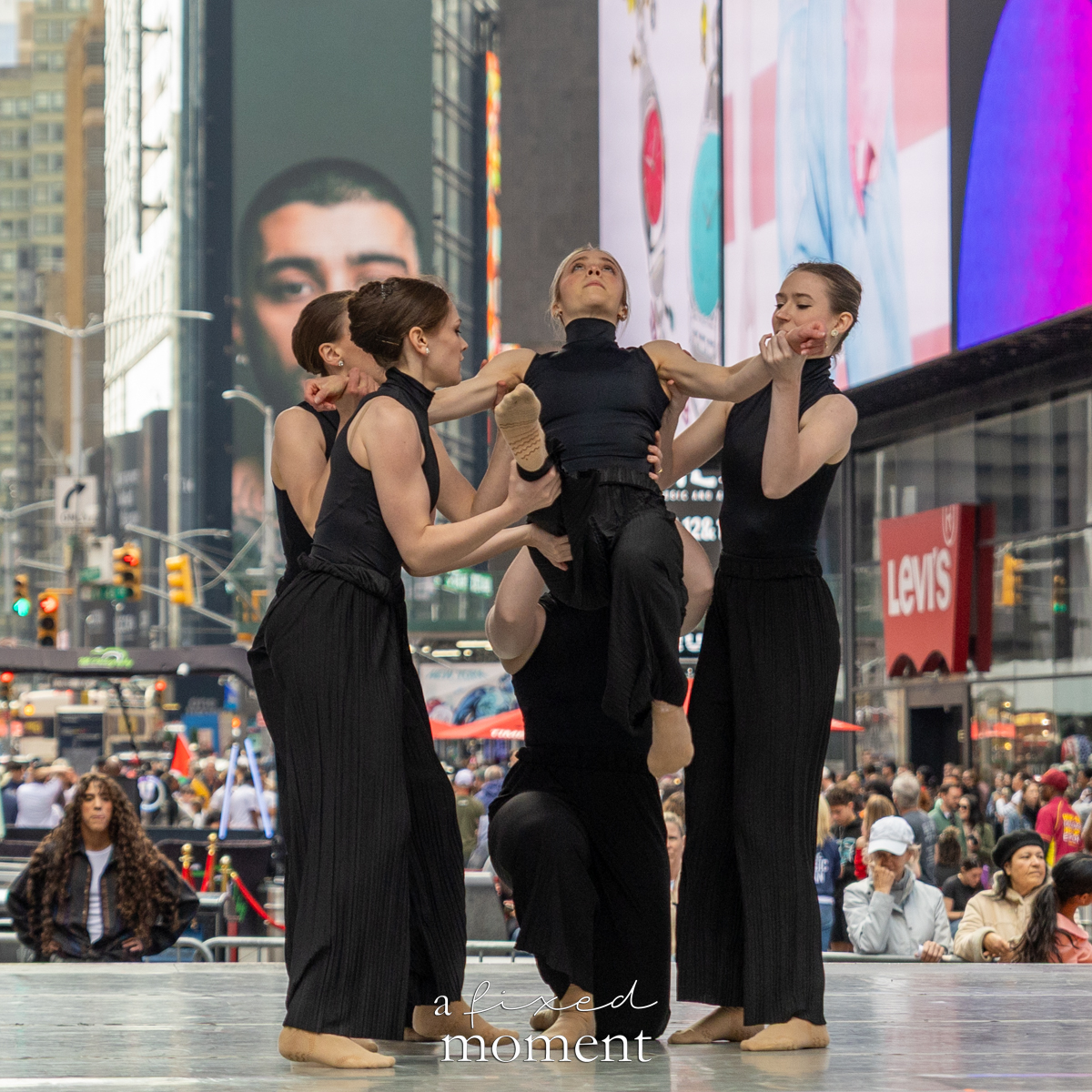 Project Dance dancers in black costumes perform a group lift on stage