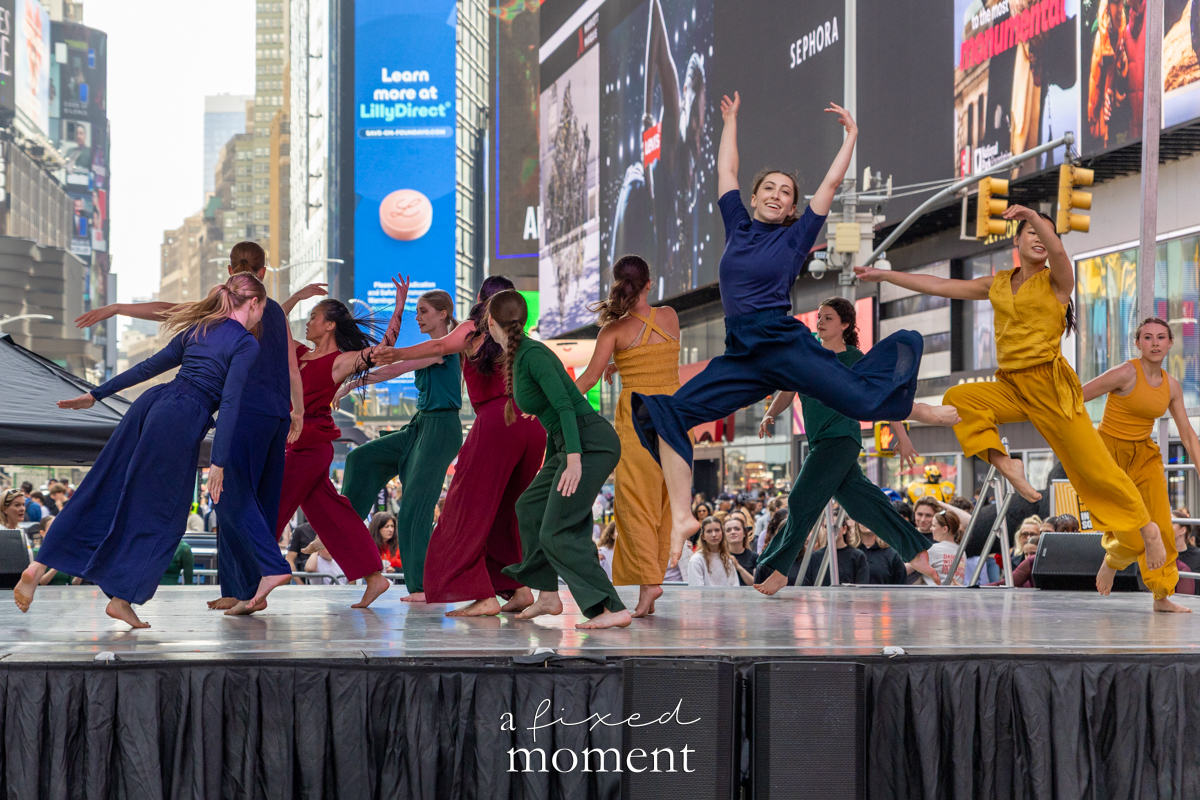Project Dance dancers leap in colorful costumes on stage in Times Square