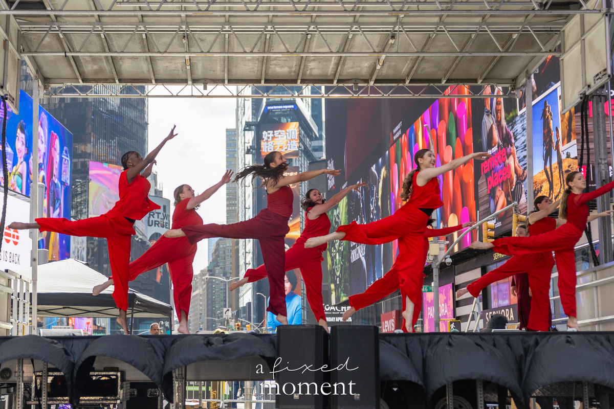 Project Dance dancers in red costumes perform a leap line on stage