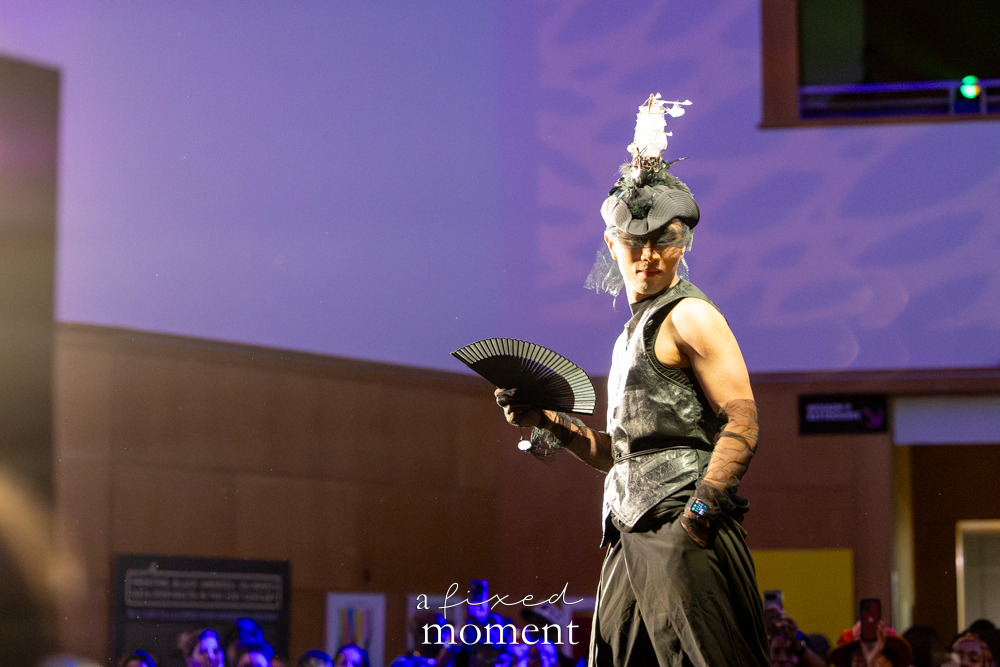 Participant with a black fan poses in a spotlight on the runway at Brooklyn's 2026 People's Ball