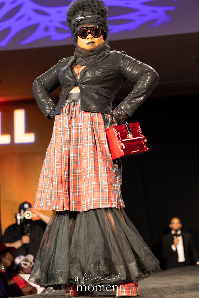 Participant in a black sequin plaid look with a red handbag on the runway at Brooklyn's 2026 People's Ball