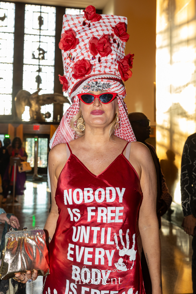 @happyeverything_art in a red political fashion look reading Nobody is free until every body is free at Brooklyn's 2026 People's Ball