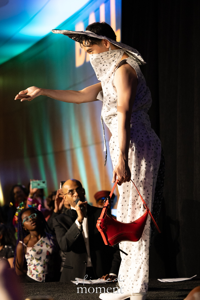 Participant in a white bandana look with a red handbag on the runway at Brooklyn's 2026 People's Ball